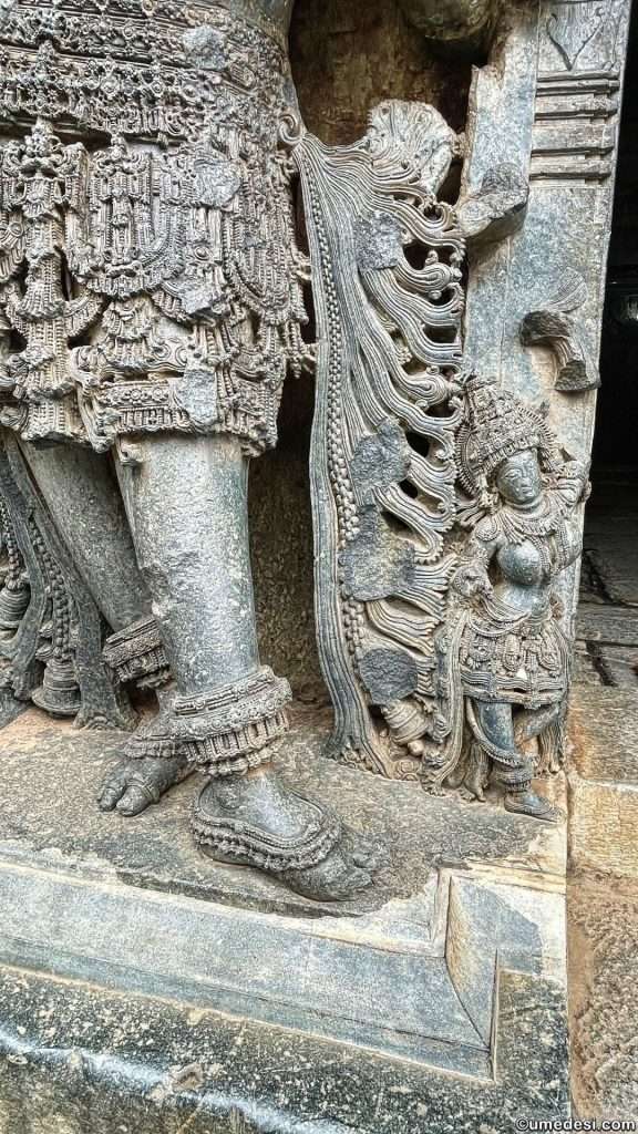 Close-up view of intricately carved drapery and jewelry on a temple sculpture at Hoysaleswara Temple.