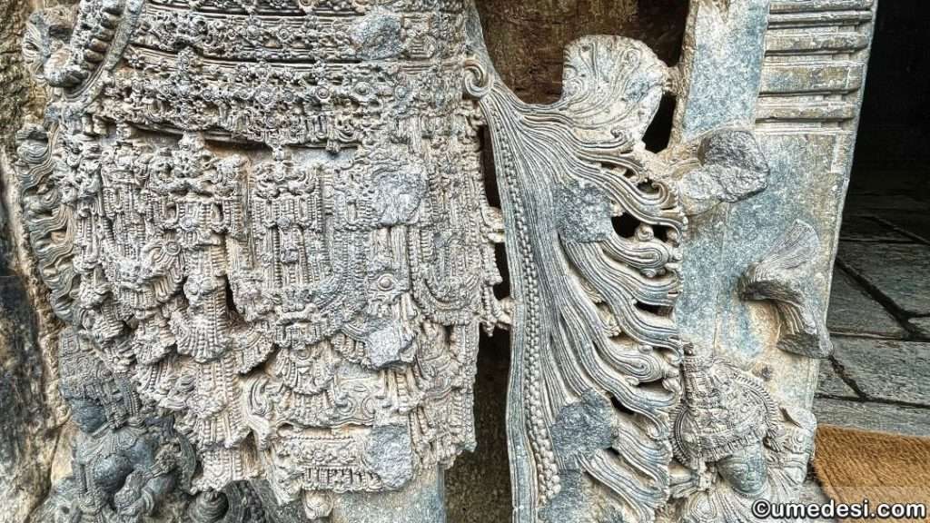 Close-up view of intricately carved drapery and jewelry on a temple sculpture at Hoysaleswara Temple.