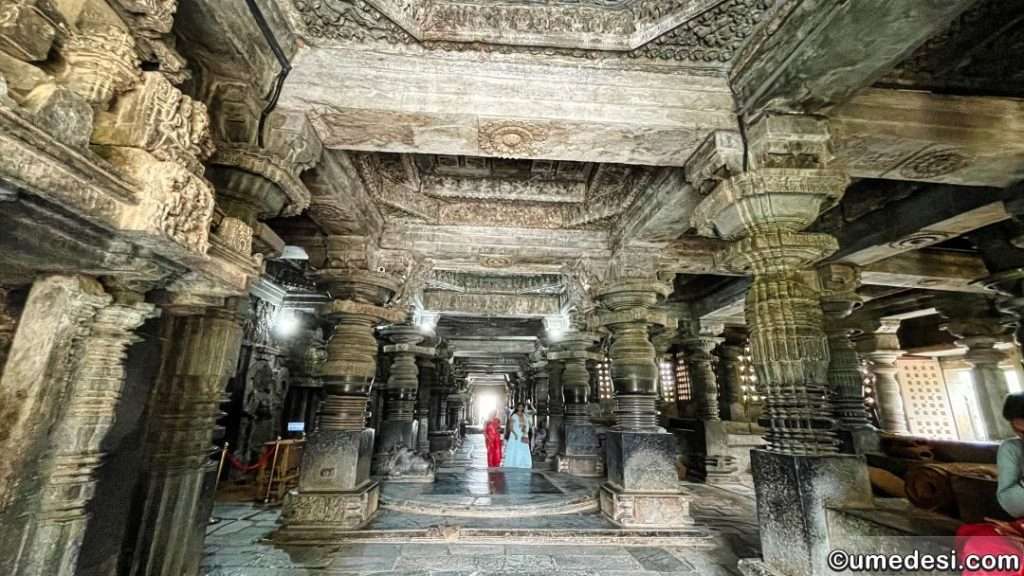 A view of the temple hall at Hoysaleswara Temple with ornate carved pillars and a richly detailed ceiling.