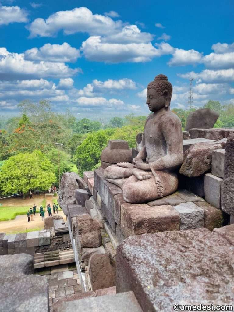 Buddha statue on the upper level of Borobudur Temple, gazing over lush green landscapes in Central Java.