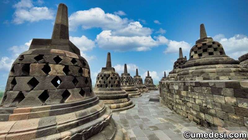 Upper terrace walkway at Borobudur Temple with a row of perforated stupas under a clear blue sky in Central Java.
