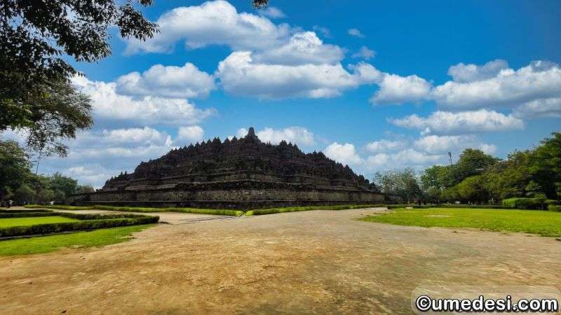 Wide-angle view of Borobudur Temple’s terraced structure against a bright blue sky, with surrounding greenery in Central Java, Indonesia.