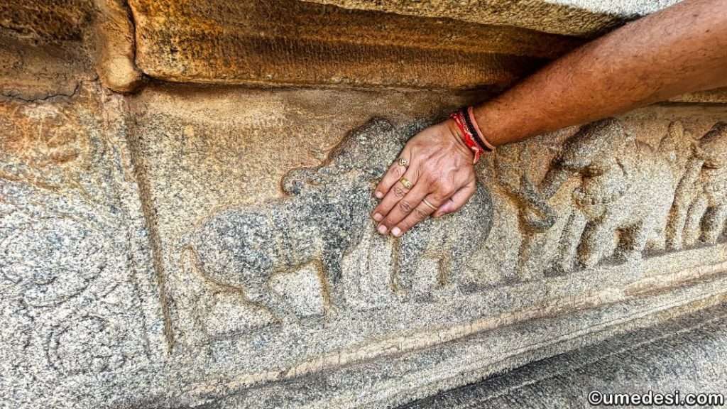 A hand touching elephant carvings on the temple wall at Vijaya Vittala Temple.