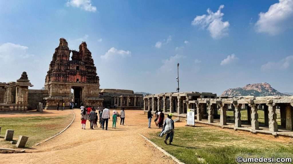 Main gopuram and mandapa at Vijaya Vittala Temple in Hampi under a bright blue sky.